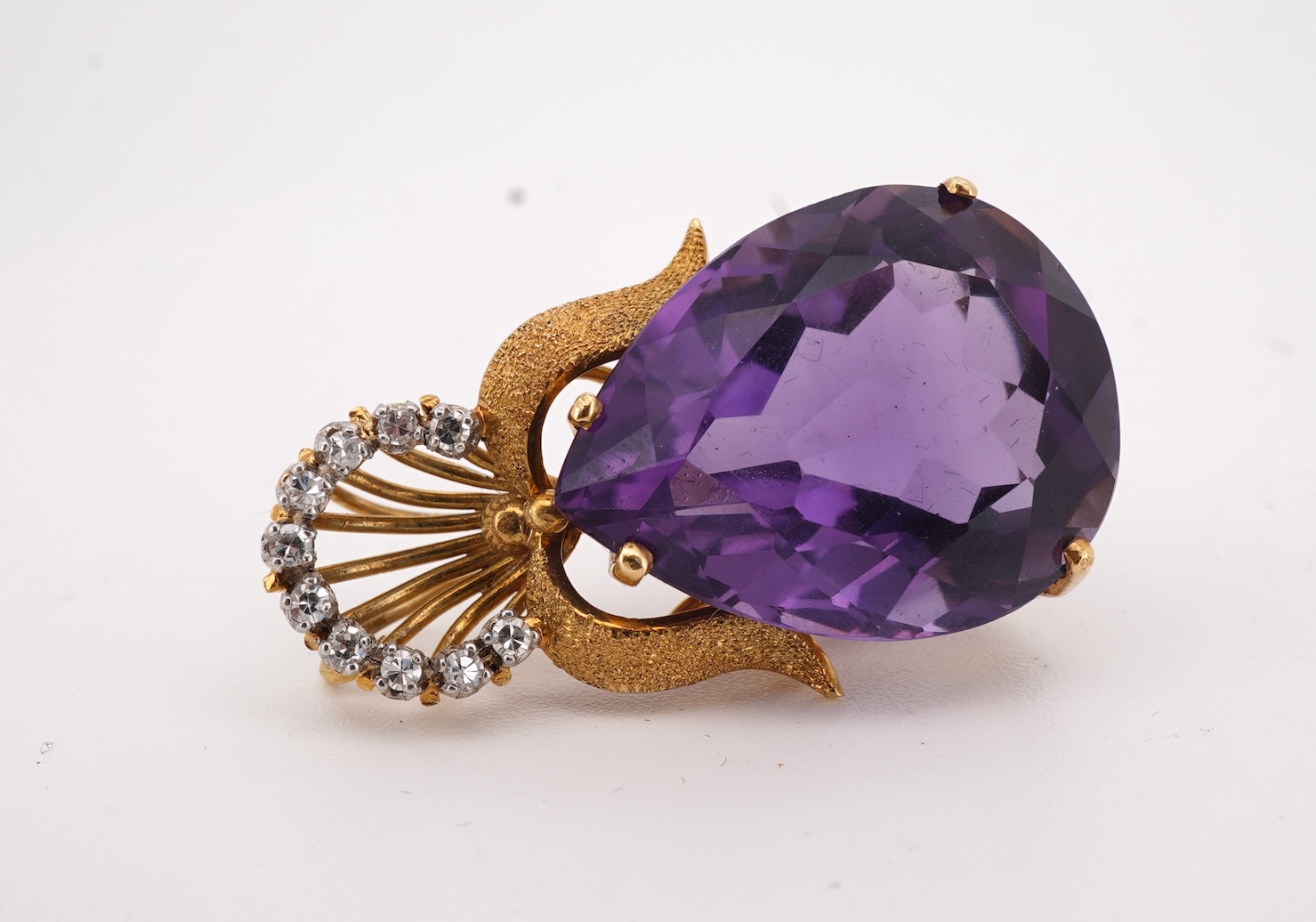 An Amethyst and diamond pendant, claw-set with a pear-shaped amethyst, topped with a foliate surmount in textured gold, accented with and arc of brilliant-cut diamonds totalling approximately 0.30 carats, length 3.5cm, s